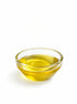 A small clear glass bowl filled with golden yellow oil, photographed on a clean white background.